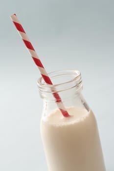 Full glass bottle of milk with a colorful spiral red and white plastic straw for a healthy drink for kids rich in calcium