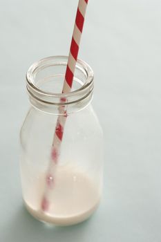 Small empty milk bottle with a colorful red striped straw and the remnants of the consumed drink in the bottom, close up high angle conceptual of a healthy diet for kids