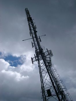 Vert tall steel lattice communications tower stretching up towards the cloudy blue sky with antennas and radio dishes mounted up its length