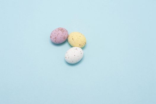 Three small sugared chocolate Mini Eggs on a blue background with plenty of copyspace for Easter