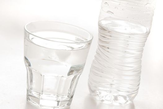 Glass of pure bottled water in a glass tumbler with a plastic water bottle behind, over white
