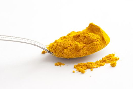 Full spoon of yellow turmeric powder spice viewed from the side in close-up on white surface