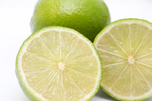Close-up of two fresh nutritious limes with one cut in two halves in front, on white background