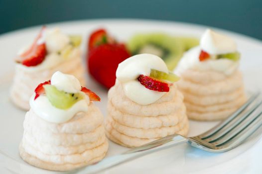 Indiviual meringue pavlovas with decorative twirled cases filled with whipped cream, strawberries and kiwi fruit