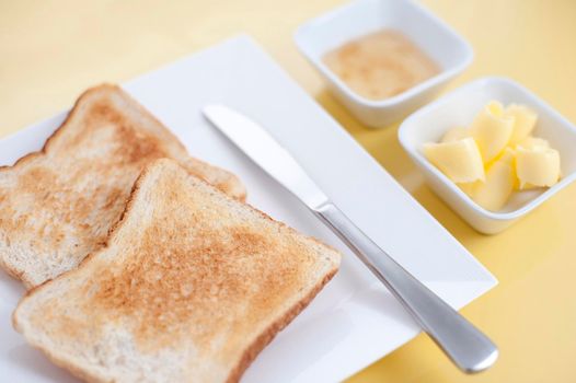 White toast on a plate served for breakfast with individual dishes of rolled butter and marmalade, high angle view