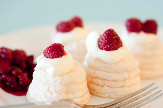 Individual mini meringue pavlovas with decorative twirled cases filled with whipped cream and topped with ripe red raspberries