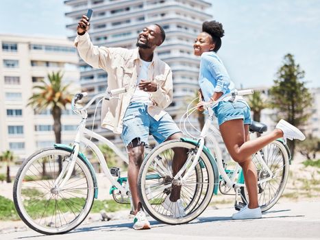 Selfie, bike and date with a couple cycling on a promenade during summer with love, romance and affection. Bicycle, photograph and fun with a black woman and man outside and a city in the background.