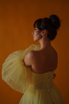 Profile portrait of a beautiful middle-aged woman in a yellow dress, her hair pulled up against a yellow background.