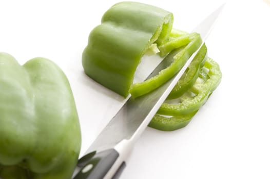 Close-up of green pepper cut in slices with knife. White background