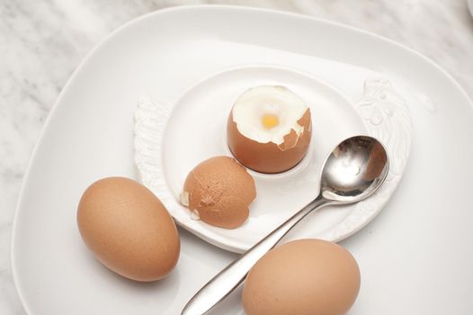 Boiled eggs for breakfast with a soft boiled egg in an egg cup served with two additional eggs on the side