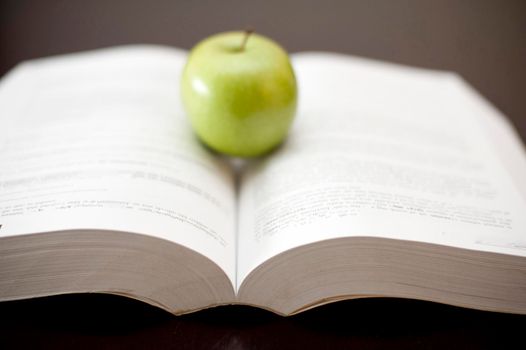 Green apple positioned on the pages of an open book. Selective focus