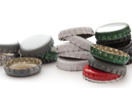 Pile of assorted metal bottle tops from bottled drinks in different colours, close up view on white with copyspace