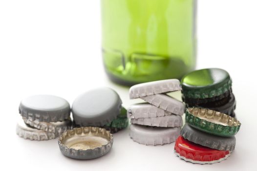 Empty green bottle with assorted different colored bottle tops stacked randomly in the foreground, close up on white