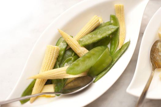 Side serving of tasty vegetables in an individual dish with mangetout or sugar snap peas and baby corncobs