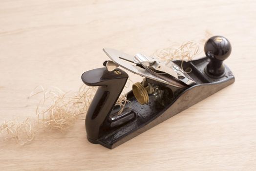 Old-fashion woodworking carpenters plane tool in close-up with wooden shavings on table surface