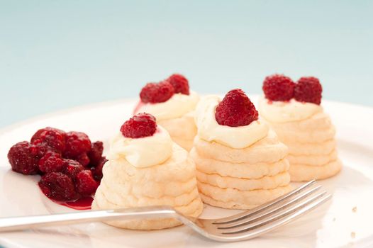 Serving on a plate of mini meringue pavlovas with decorative twirled cases filled with whipped cream and raspberries