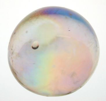 Iridescent toy glass marble viewed close up showing the colorful internal refraction of light over white