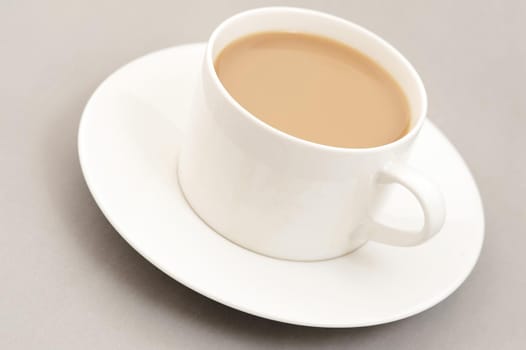 Cup of white milky coffee in a modern generic white cup and saucer viewed high angle close up over a beige background