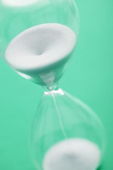 Close up view of hour glass with white sands pouring into lower part against a green background
