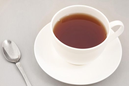 Cup of freshly brewed black tea in a generic white ceramic cup and saucer with a teaspoon alongside, high angle view