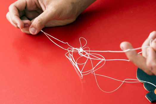 Fixing a problem concept by untangling a knot with a closeup view of hands of a man unravelling a badly knotted piece of string over a red background