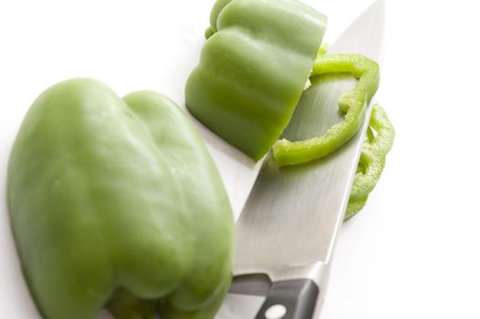 Slices of fresh green capsicum or bell pepper resting on the blade of a sharp kitchen knife during preparation for use in salads