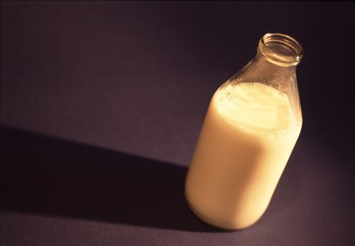 Glass bottle of cows milk with the top off on a black background with copyspace