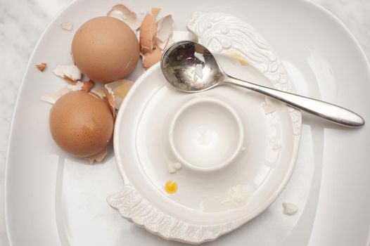 View from above of an empty egg cup with two overturned eggshells from two boiled eggs that have been consumed for breakfast