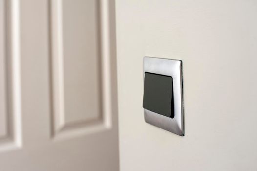 Modern silver framed plastic light switch on a white wall alongside a white painted wooden paneled door