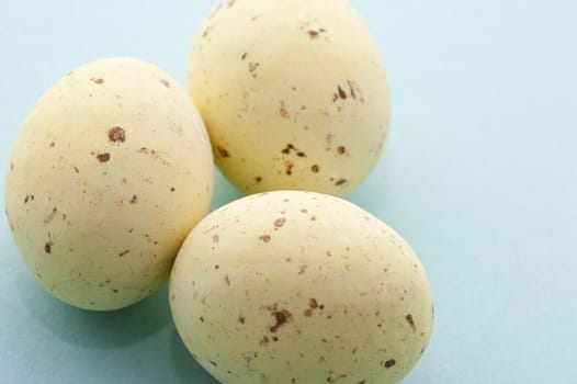 Closeup of pastel yellow speckled mini Easter Eggs on a blue background with copyspace
