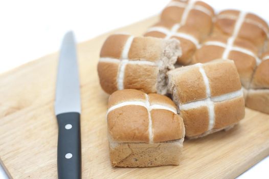 Fresh batch of Easter Hot Cross Buns on a wooden board with a knife