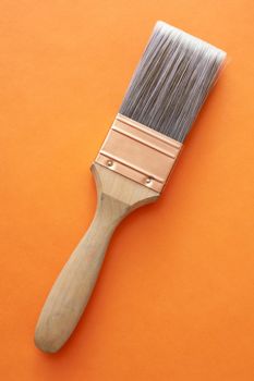 Single large wooden and copper paintbrush placed over orange background at an angle