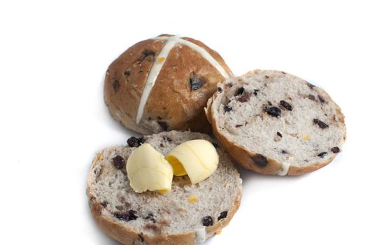 Sliced and buttered spicy fruity Hot Cross bun for Easter with a whole one behind showing the symbolic pastry cross over a white background