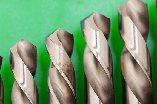 Close up of the tips of a set of metal steel spiral woodworking drill bits in descending size on a green background with copyspace