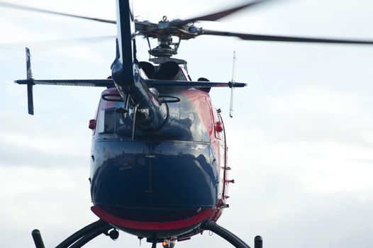 Helicopter taking off on a flight viewed from below the tail looking at the fuselage against a cloudy sky