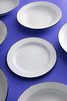 Clean empty white enamelled metal kitchen plates on a bright blue surface scattered randomly viewed high angle