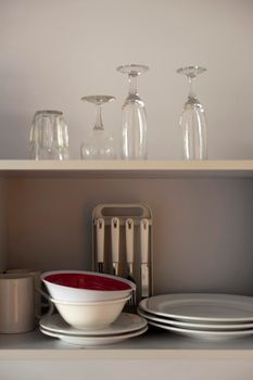 Assorted crockery and glassware stacked on an open wooden kitchen shelf