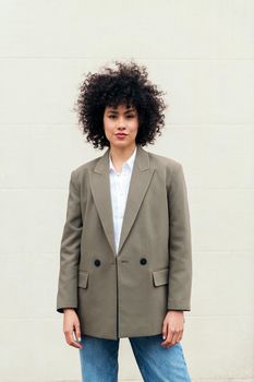 stylish business woman with curly hair wearing a blazer and looking at camera, concept of success and youth