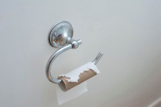 Toilet paper holder on white wall with an empty roll of paper