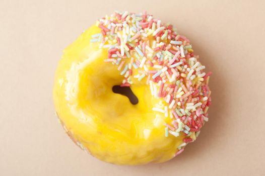 Glazed lemon ring doughnut with colorful citrus icing dipped in multicolored sprinkles on one side, overhead view on a neutral background