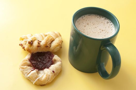 High angle view of a frothy mug of cappuccino coffee with two fresh pastries or biscuits on a yellow background