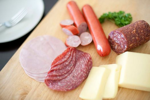 Nourishing German breakfast with sliced spicy salami or pepperoni sausage, cold ham and sliced cheese on a wooden chopping board