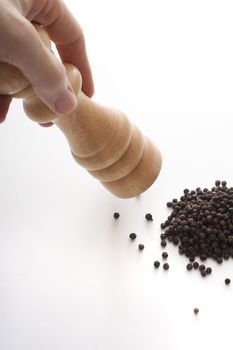 Milling black pepper with wooden mill. Close-up view against white surface background