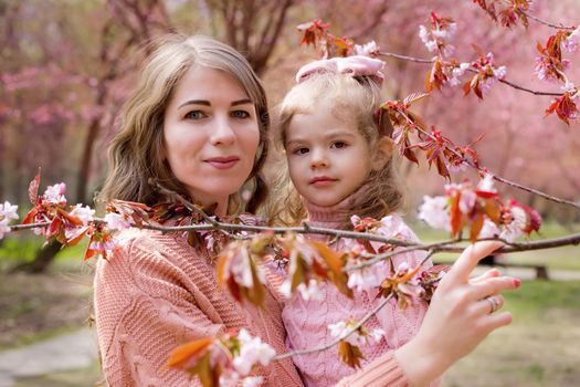 Portrait of beautiful mother and daughter in the park with blooming pink sakura. Close up
