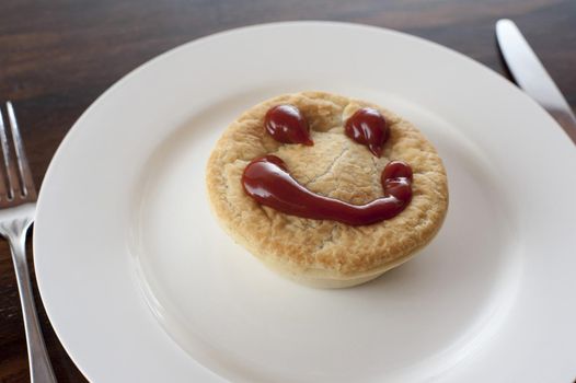 Meat pie with a happy face made of tasty sauce on top of the pastry crust served on a plain white plate