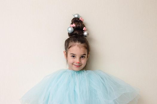 Portrait of funny beautiful girl with a hairstyle in the form of a Christmas tree , in blue clothes , stands against the background of a light wall