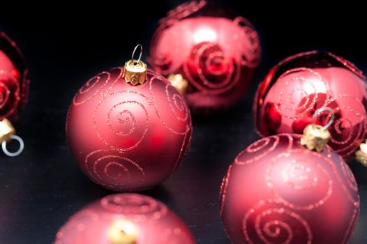 Red Christmas ornamental baubles with glitter curlicues on a dark background