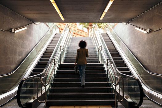 rear view of the silhouette of an unrecognizable business woman walking up the stairs of the subway station with a briefcase in her hand, concept of urban lifestyle and growth