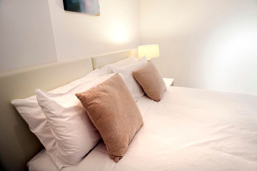 Close up of a modern bedset with neutral decor in tones of brown, beige and white illuminated by bedside lamps