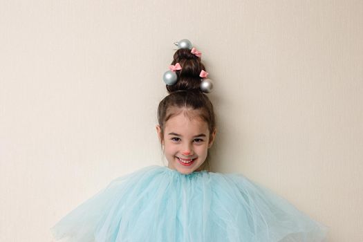 Portrait of funny beautiful girl with a hairstyle in the form of a Christmas tree , stands against the background of a light wall